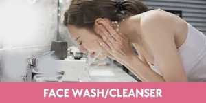 "A clear bottle of facial cleanser with a blue pump, labeled 'Face Wash/Cleanser,' placed on a marble bathroom counter with fresh water droplets glistening on its surface."